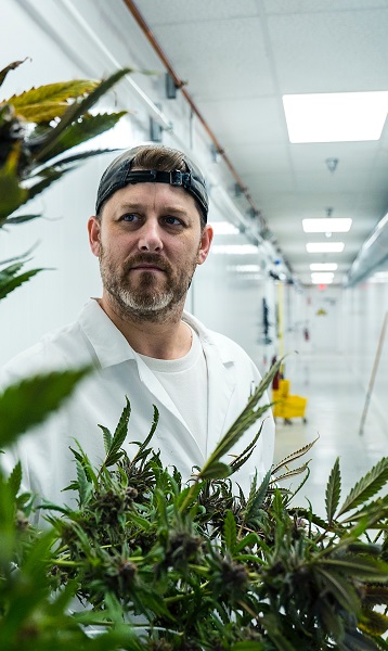 A worker moving product with cleaning supplies in the background in a cannabis cultivation facility.